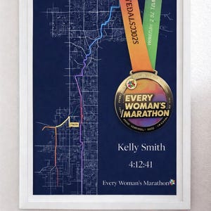 May include: Framed navy blue map art with a marathon medal. The medal reads "Every Woman's Marathon" and includes the runner's name and time. Pink running shoes are in the foreground. The map shows the race route.