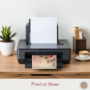 Op de afbeelding: Een zwarte desktop-printer met een leeg wit vel papier in de bovenste lade en een bedrukte kaart in de uitvoerlade. De kaart bevat een roze roosillustratie en de tekst "God is Love" in een cursief lettertype op een lichtbeige achtergrond.