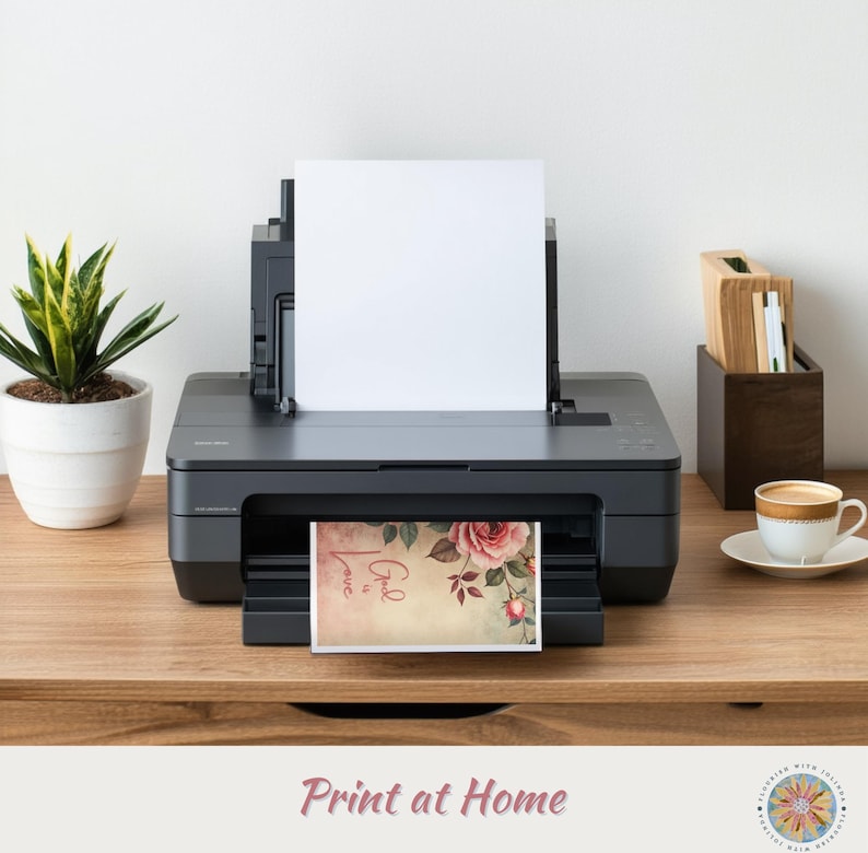 Op de afbeelding: Een zwarte desktop-printer met een leeg wit vel papier in de bovenste lade en een bedrukte kaart in de uitvoerlade. De kaart bevat een roze roosillustratie en de tekst "God is Love" in een cursief lettertype op een lichtbeige achtergrond.