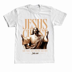 Puede incluir: Camiseta blanca con un gráfico de Jesucristo con los brazos levantados. El texto "JESUS CHRIST" está encima de la imagen, con "THE WAY, THE TRUTH, THE LIFE" y Juan 14:6 debajo.