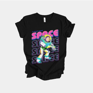 May include: Black t-shirt featuring a colorful graphic of Buzz Lightyear from Toy Story. The design includes the phrase "I need some SPACE" in pink and blue, with the word "SPACE" repeated vertically. The cartoon character is in a dynamic pose.