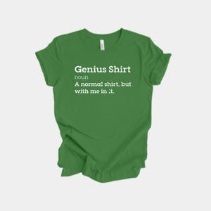 Puede incluir: Una camiseta verde con el texto "Genius Shirt" en blanco, seguida de una definición. La definición dice: "Una camiseta normal, pero conmigo dentro."