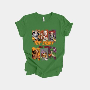 May include: Green t-shirt featuring a graphic design with characters dressed in Halloween costumes. The design includes the text "TOY STORY EST. 1995". The shirt is made of a soft material.
