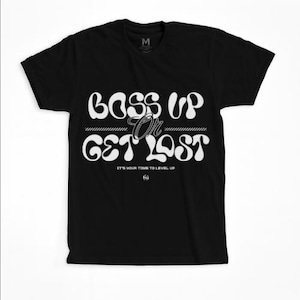 May include: Black t-shirt with the words "BOSS UP OR GET LOST" in a white, stylized font. The shirt also includes the text "IT'S YOUR TIME TO LEVEL UP" in a smaller font. A small "M" logo is visible near the collar.