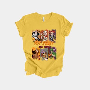 May include: Yellow t-shirt featuring a graphic of Toy Story characters dressed in Halloween costumes. The design includes a skeleton Woody, Buzz Lightyear, and Jessie. The text "TOY STORY EST. 1995" is also printed on the shirt.