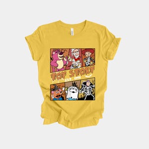 K&ouml;nnte beinhalten: Gelbes T-Shirt mit einem Toy Story-Motiv. Das Design zeigt Charaktere wie Lotso, Woody und andere in Halloween-Kost&uuml;men. Der Text "Toy Story Est. 1995" ist ebenfalls enthalten.