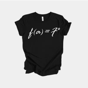 May include: Black t-shirt featuring the white text "f(a) = 7°" in a handwritten font. The t-shirt has a crew neck and is made of a soft fabric. The garment is folded.
