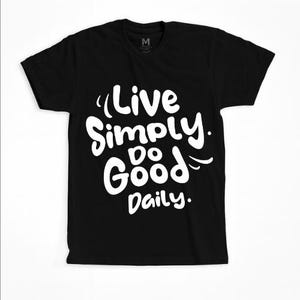 Puede incluir: Camiseta negra con el texto blanco "Live Simply. Do Good Daily." La camiseta tiene cuello redondo y mangas cortas. El texto está en un estilo manuscrito.