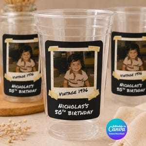 May include: A clear plastic party cup featuring a rectangular black label with a vintage-style photo of a young child. The label includes the text Vintage 1976 and Nicholas's 50th Birthday, with the photo appearing to be taped on with tan adhesive strips.
