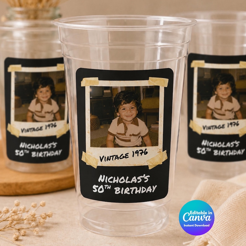 May include: A clear plastic party cup featuring a rectangular black label with a vintage-style photo of a young child. The label includes the text Vintage 1976 and Nicholas's 50th Birthday, with the photo appearing to be taped on with tan adhesive strips.