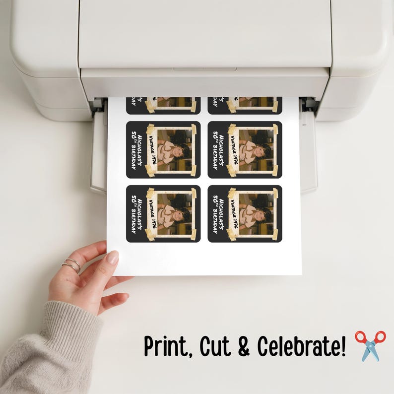 May include: A white sheet of paper emerging from a printer, featuring four identical rectangular stickers. Each sticker has a black background, a central photograph of a child, and white text reading "NICHOLAS'S 50TH BIRTHDAY" and "VINTAGE 1976".