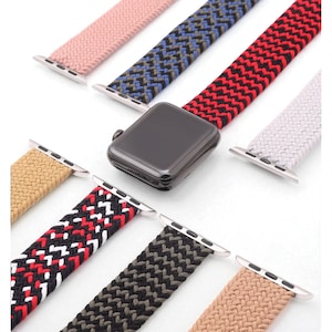 Puede incluir: Un reloj inteligente negro con varias correas de reloj tejidas de colores. Las correas incluyen rosa, azul, rojo, blanco, beige, negro y blanco, negro y gris y beige. Cada correa tiene conectores plateados.