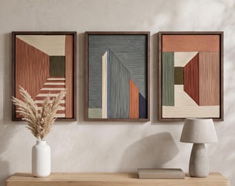 May include: A set of three rectangular wall art pieces in dark wood frames, each featuring textured, layered geometric patterns in shades of terracotta, cream, sage green, and slate blue, displayed above a wooden console table.