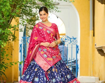 May include: A traditional Indian outfit featuring a vibrant pink and blue lehenga. The skirt is a deep blue with a patterned design, and the top and shawl are a bright pink with intricate detailing. The outfit is accented with gold jewelry.