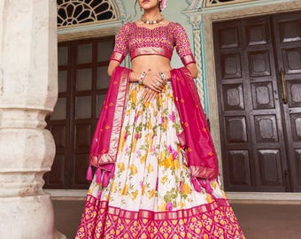 May include: A traditional Indian outfit featuring a pink embroidered crop top and a matching skirt. The skirt has a floral print on a white background, with a geometric patterned border. A pink scarf is draped over the shoulders.