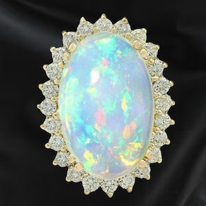 May include: An oval opal gemstone ring with a halo of small diamonds set in gold. The opal has a milky white base with flashes of blue, green, and pink. The ring is set against a black background.