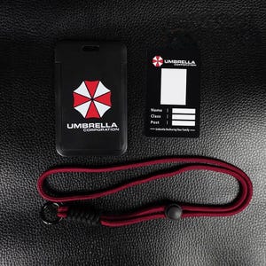 Black Umbrella badge holder with inner card and red rope lanyard on leather background, access card cover.