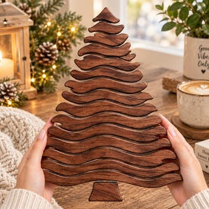 May include: A decorative wooden Christmas tree ornament featuring a layered, wavy design with a dark brown wood grain finish. The object is shaped like a stylised evergreen tree with a flat base and horizontal, undulating segments stacked vertically.