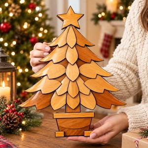 Könnte beinhalten: Ein dekorativer Weihnachtsbaumschmuck aus Holz mit geschichteten, blütenblattförmigen Zweigen in verschiedenen hellen und mittleren Brauntönen, gekrönt von einem fünfzackigen Stern und auf einem rechteckigen Holzsockel.