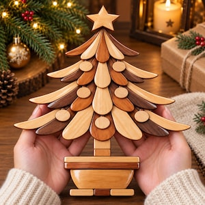 May include: A decorative wooden Christmas tree ornament featuring layered, teardrop-shaped branches in varying shades of light, medium, and dark brown wood. The tree is topped with a five-pointed star and sits in a rectangular wooden base.