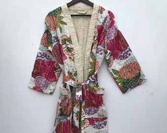 May include: A long, quilted robe with a floral pattern in shades of pink, orange, green, and white. The robe has a cream-colored interior and a matching belt. The robe is hanging on a wooden hanger.