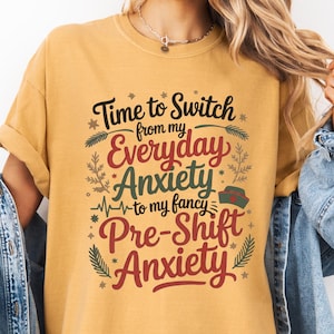 May include: Mustard yellow t-shirt with the text "Time to Switch from my Everyday Anxiety to my fancy Pre-Shift Anxiety" in a decorative font. The shirt has a crew neck and short sleeves. The text is in a mix of colors, including red, green, and black.
