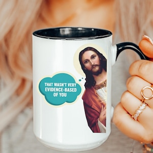 May include: White ceramic mug with a black rim and handle. The mug features an image of Jesus with a speech bubble that reads, "THAT WASN'T VERY EVIDENCE-BASED OF YOU."
