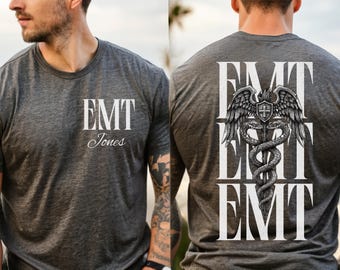 Puede incluir: Camiseta gris oscuro con el texto "EMT Jones" en la parte delantera. La parte trasera de la camiseta presenta el texto "EMT" con un símbolo de Caduceo. El símbolo del Caduceo tiene alas, una cruz y dos serpientes enrolladas alrededor de un bastón.
