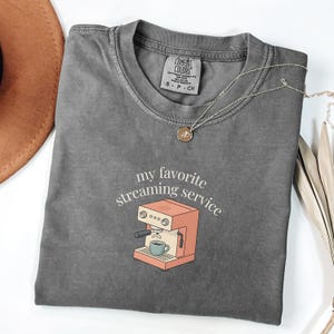 May include: A set of three ceramic mugs with a speckled, matte finish. Each mug features a different color: light blue, cream, and gray. The mugs have a simple, modern design with a rounded shape and a comfortable handle.