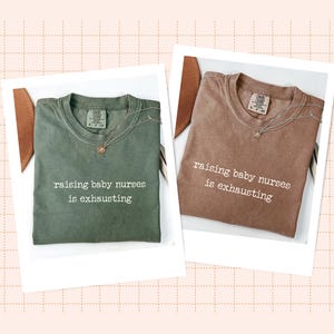 May include: Two t-shirts, one olive green and one brown, each with the phrase "raising baby nurses is exhausting" printed in white. Each shirt is paired with a delicate necklace. The shirts are displayed on a white background.