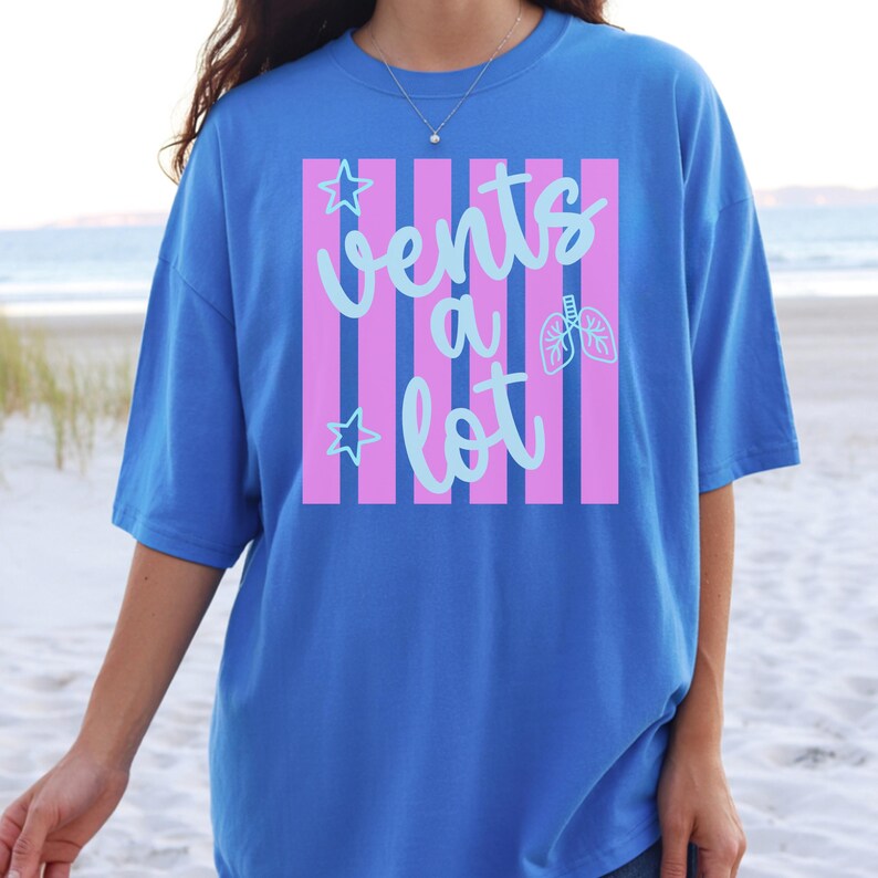 Puede incluir: Una camiseta azul con la frase "Vents a lot" en escritura azul claro, sobre un fondo a rayas rosas y blancas. El dise&ntilde;o incluye estrellas y gr&aacute;ficos de pulmones. La camiseta es de estilo casual y manga corta.