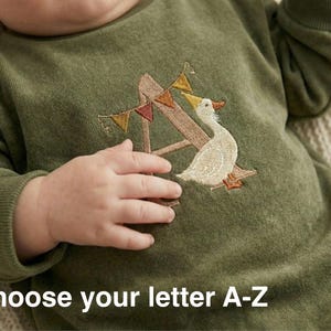 Könnte beinhalten: Olivgrüner Baby-Overall mit gesticktem Buchstaben "A" und einem Gänsemotiv. Der Overall hat ein dekoratives Banner und den Text "Choose your letter A-Z".