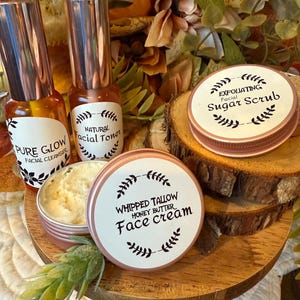 May include: A collection of skincare products, including facial cleanser, toner, sugar scrub, and face cream. The products are in small, round, and cylindrical containers with rose gold lids and labels. The labels feature text and botanical illustrations. The products are arranged on a wooden tray.