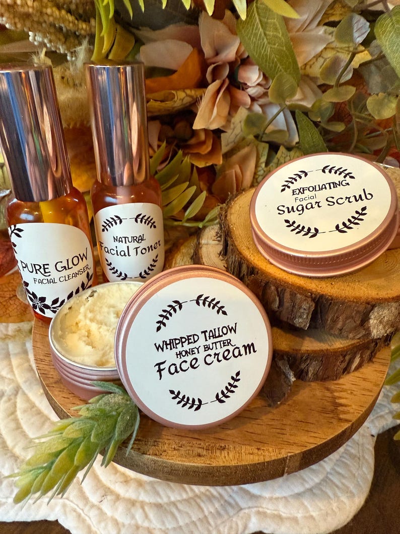 May include: A collection of skincare products, including facial cleanser, toner, sugar scrub, and face cream. The products are in small, round, and cylindrical containers with rose gold lids and labels. The labels feature text and botanical illustrations. The products are arranged on a wooden tray.