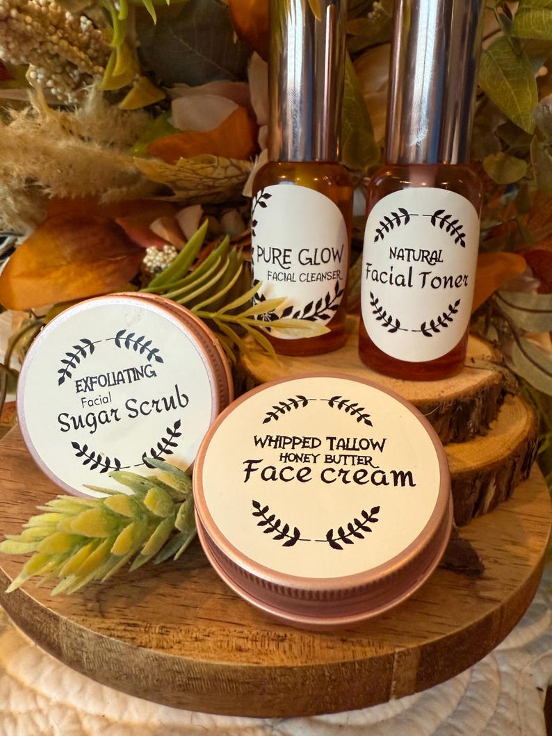 May include: A collection of skincare products, including facial cleanser, toner, sugar scrub, and face cream. The products are in small glass bottles and round tins with labels. The labels feature botanical illustrations and product names.