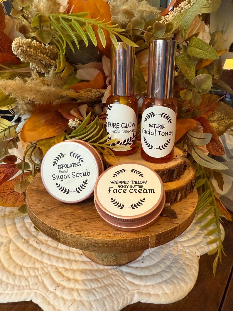 May include: A display of skincare products, including two glass bottles with silver tops labeled "Pure Glow" and "Natural Facial Toner." Two round containers are labeled "Exfoliating Facial Sugar Scrub" and "Whipped Tallow Honey Butter Face Cream."