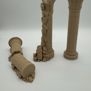 Könnte beinhalten: Drei beige, einfarbige Miniatursäulen mit ägyptischen Hieroglyphen und lotusförmigen Kapitellen. Eine Säule steht aufrecht, eine ist teilweise zerbrochen und eine liegt horizontal auf einem Haufen trümmerartiger Bruchstücke.