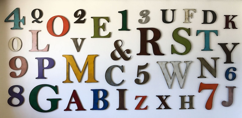 Puede incluir: Una colecci&oacute;n de letras y n&uacute;meros de madera coloridas en varios tama&ntilde;os y fuentes. Las letras y los n&uacute;meros est&aacute;n pintados en tonos de rojo, verde, azul, amarillo y marr&oacute;n. La disposici&oacute;n est&aacute; sobre un fondo blanco.