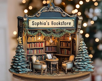 May include: A detailed Christmas ornament depicting "Sophia's Bookstore." The ornament features a miniature bookstore interior with bookshelves, chairs, a table, and two small Christmas trees. The sign above reads "Sophia's Bookstore."