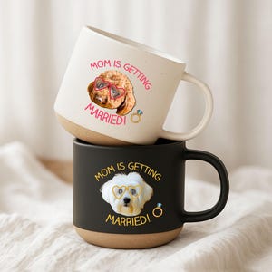 May include: Two ceramic mugs stacked on top of each other. The top mug is white with a brown base and a handle. It has a dog graphic wearing heart-shaped glasses and the text "MOM IS GETTING MARRIED!". The bottom mug is black with a brown base and a handle. It has a dog graphic wearing heart-shaped glasses and the text "MOM IS GETTING MARRIED!"