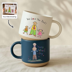 May include: Two ceramic mugs stacked on top of each other. The top mug is white with a drawing of a family and the text "We Love You Dad!". The bottom mug is blue with a drawing and the text "Happy Father's Day".