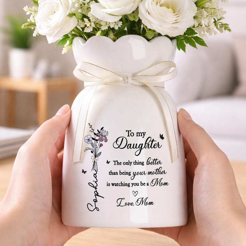 May include: White ceramic vase with a scalloped rim, tied with a cream-colored ribbon, and filled with white flowers. The vase has a floral design and the text "To my Daughter" with a personalized name and message.