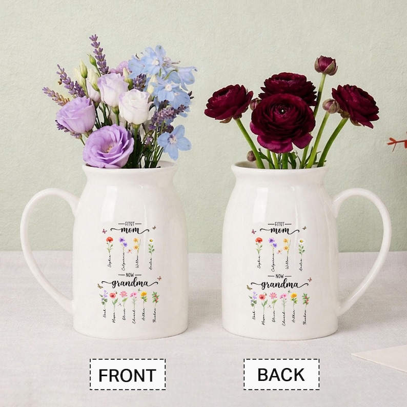 K&ouml;nnte beinhalten: Zwei wei&szlig;e Keramikvasen mit Griffen, jede mit Blumen. Eine Vase hat lila, wei&szlig;e und blaue Blumen, die andere dunkelrote Blumen. Auf den Vasen steht "First Mom - Now Grandma" mit Namen darunter.