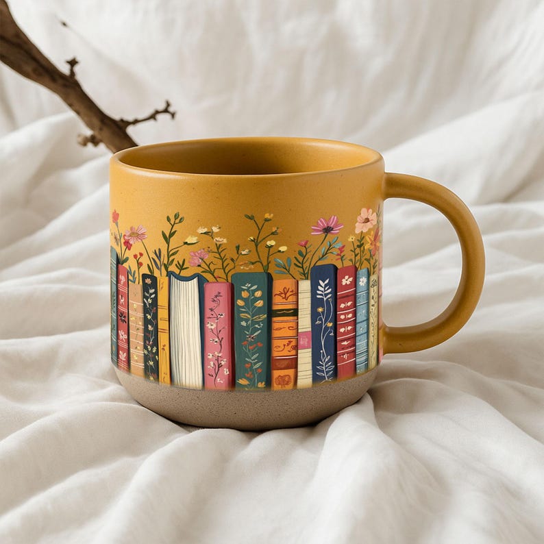 May include: Mustard yellow ceramic mug featuring a design of colorful books with flowers growing from the top. The mug has a tan base and a matching handle. The books have various floral and patterned designs.