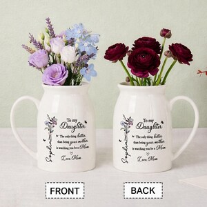 May include: Two white ceramic vases with handles, each holding flowers. One vase has purple, white, and blue flowers, the other has dark red flowers. Text on the vases reads "To My Daughter" and "Love Mom."