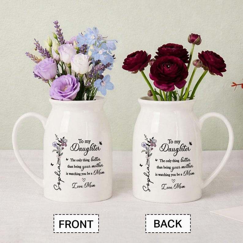 May include: Two white ceramic vases with handles, each holding flowers. One vase has purple, white, and blue flowers, the other has dark red flowers. Text on the vases reads "To My Daughter" and "Love Mom."