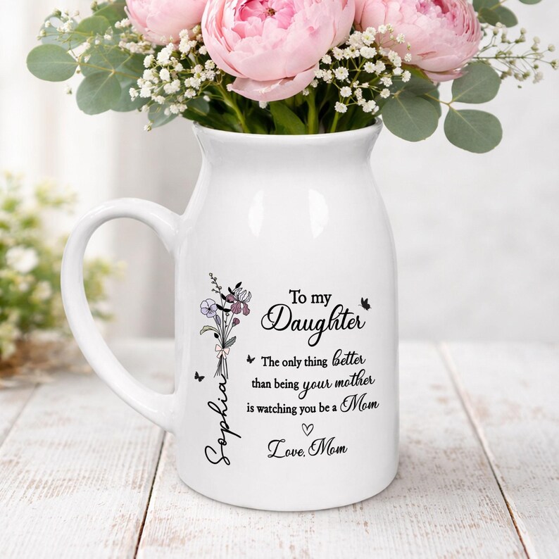 May include: White ceramic pitcher with a handle, featuring a floral bouquet and the text "To my Daughter". The pitcher holds pink peonies and greenery. The text includes "Sophia", "Love, Mom", and a heart symbol.