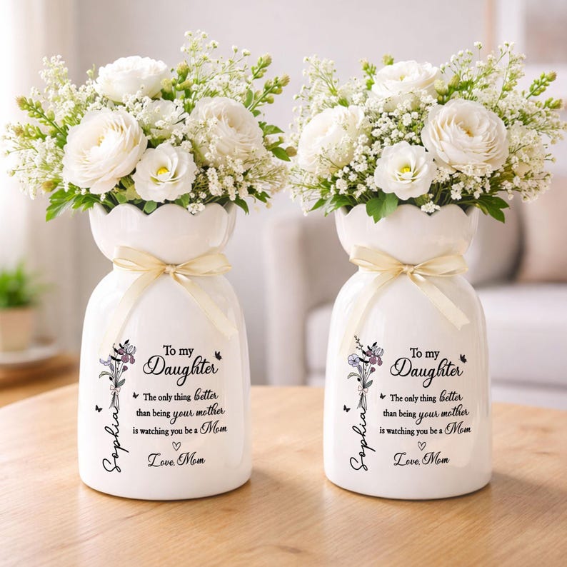 May include: Two white ceramic vases, each holding a bouquet of white flowers and greenery. The vases have a scalloped rim, a cream-colored ribbon, and a printed message: "To my Daughter" with a personalized name and a loving message.