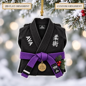 Può includere: Un ornamento piatto in acrilico 2D a forma di gi da jiu-jitsu nero con una cintura viola. Il gi presenta il nome AVA, caratteri giapponesi e l'anno 2026. Una medaglia circolare color oro pende dalla cintura insieme a un rametto di pino.