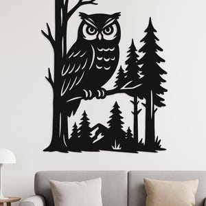 Op de afbeelding: Zwarte metalen wandkunst met een uil op een tak, tegen een bosachtergrond. De uil heeft gedetailleerde veren en grote ogen. Het kunstwerk is gemonteerd op een witte muur boven een grijze bank.
